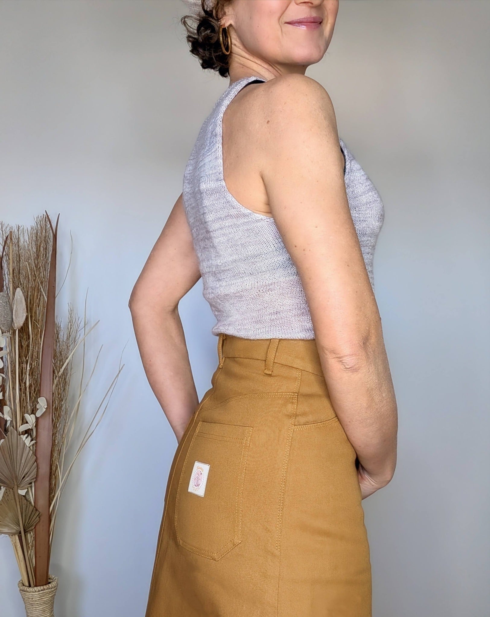 Jupe en jean camel taille haute portée par une femme, vue de profil arrière, avec un top gris. Tag sur la poche arrière.